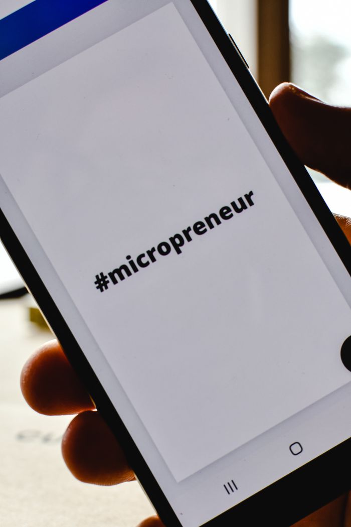 about-us-01 Close-up of a hand holding a smartphone with the hashtag #micropreneur on screen, symbolizing entrepreneurship.